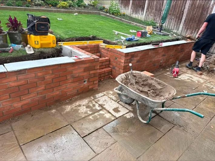 A red-brick garden wall being built with coping stones set along the top, in a domestic back garden